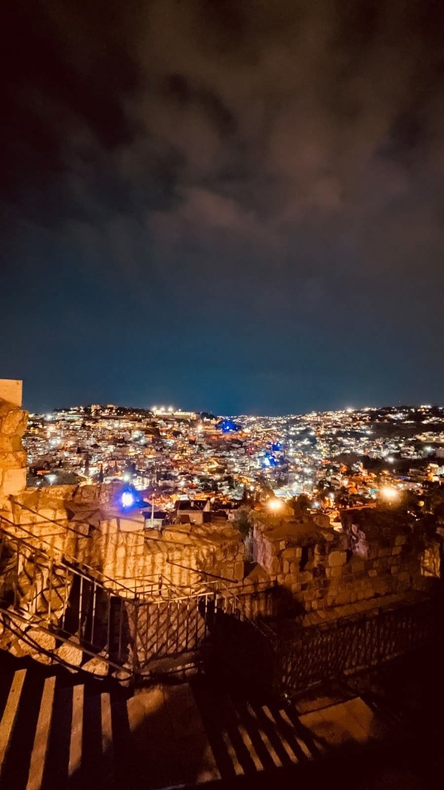 A nighttime city view beyond stone walls and steps.