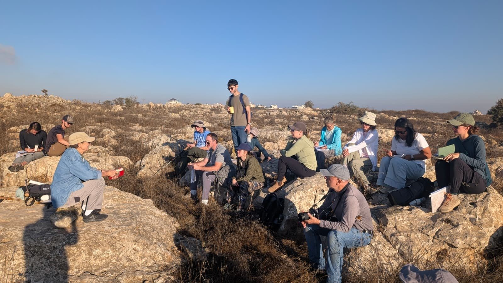 Students sit on rocky terrain during a Physical Settings field study in Samaria.